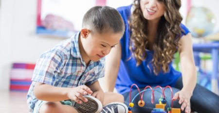 Hispanic Down Syndrome boy reaching for toys at daycare center Hispanic Down Syndrome boy reaching for toys at daycare center